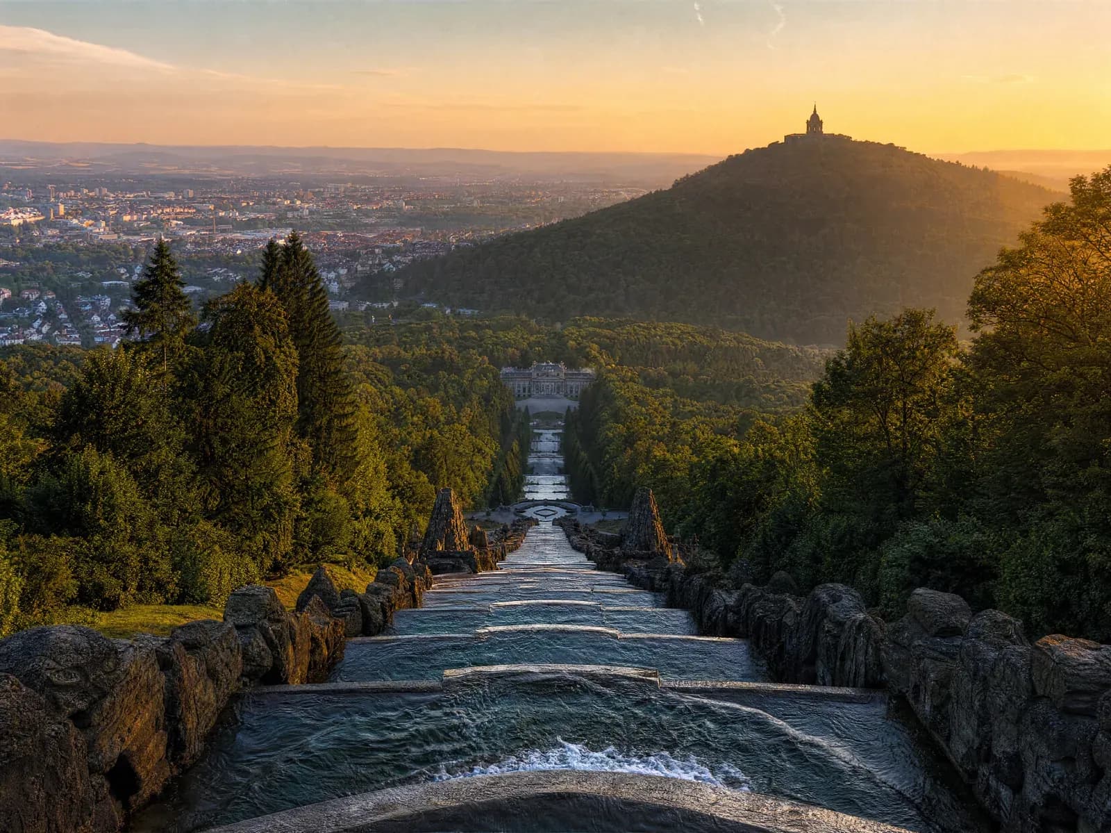 Bergpark Wilhelmshöhe in Kassel im Abendlicht, die Kaskaden führen ins Tal, der Herkules als Silhouette auf dem Hügel.